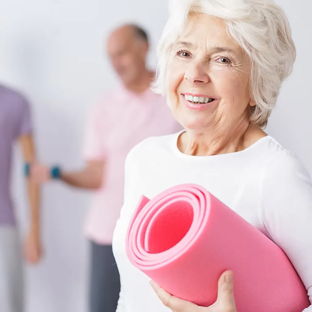 senior woman holding a rolled up pink yoga mat